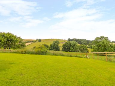 A grassy field with wooden fencing and trees in the background at The Old Farmhouse Upper Pitts in Knighton