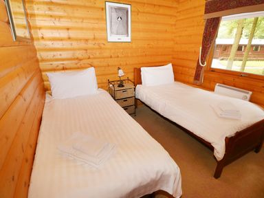 A bedroom with two single beds wooden walls a window and a small nightstand with a lamp at Lodge 8 Louth