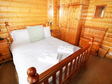 A bedroom with a wooden bed with white bedding and towels on it and wooden wardrobes and cabinets at Lodge 8 in Louth