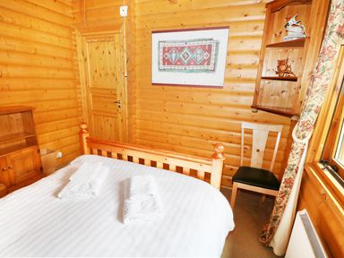 A bedroom with a wooden bedframe white bed linens and towels a wooden chair a door and a wooden shelf at Lodge 8 in Louth