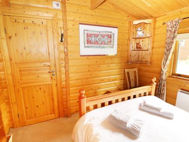 A bedroom with wooden walls a bed with folded towels a door a wooden chair a wall shelf and a window with floral curtains at Lodge 8 in Louth