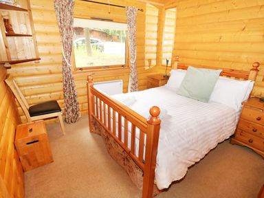A bedroom with a wooden double bed a chair a window with curtains and wooden furniture at Lodge 8 in Louth