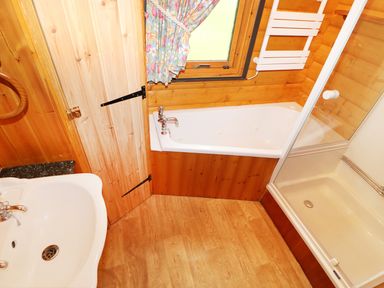 A bathroom with a sink, bathtub, shower, wooden walls and floor, and a window with floral curtains at Lodge 8 in Louth