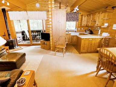 A wooden living room and kitchen area with chairs, a table, a television, and a wood stove at Lodge 8 in Louth