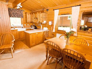 A kitchen and dining area with wooden cabinets a table with chairs and curtains at Lodge 8 in Louth