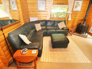 A living room with a dark green leather sectional sofa and ottoman with light cushions and wooden side tables at Lodge 8 in Louth