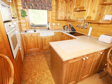 A small kitchen with wooden cabinets a sink electric stove microwave dishwasher kettle and toaster at Lodge 8 in Louth