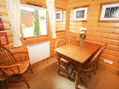 A wooden dining table with four chairs and a vase of flowers by a window in a log cabin at Lodge 8 in Louth