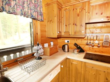 A kitchen corner with wooden cabinets a window with floral curtains a drying rack and kitchen utensils at Lodge 8 in Louth