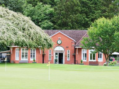 A red brick building with a clock above the entrance and two benches outside surrounded by trees and a lawn with golf flags at Lodge 8 in Louth