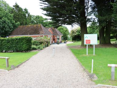 A gravel driveway leading to a small brick building surrounded by trees and greenery with a sign for Kenwick Park Golf Club at Lodge 8 in Louth