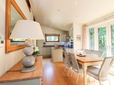 A dining area with a wooden table and wicker chairs next to glass doors with a kitchen in the background at Brooke in Exton Rutland