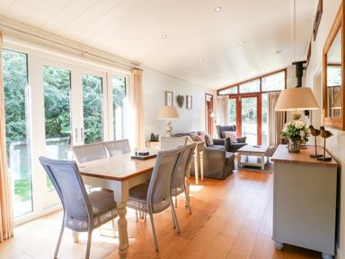 A dining area with a wooden table and six chairs next to large windows and a living area with armchairs and a coffee table at Brooke in Exton Rutland