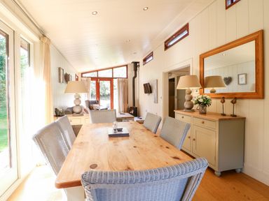 A dining area with wicker chairs and a wooden table next to a sideboard with lamps and a mirror at Brooke in Exton Rutland