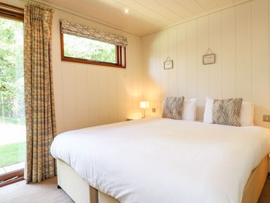 A bedroom with a large bed two patterned cushions a bedside lamp and a small window with curtains at Brooke in Exton Rutland