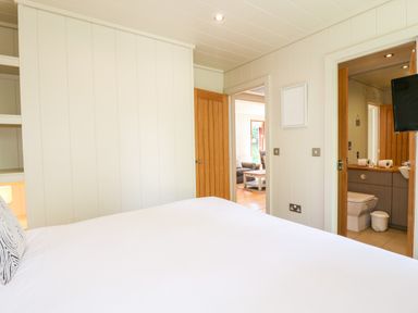 A bedroom with a white bed and pillow with two open doors showing a bathroom and living room at Brooke in Exton Rutland