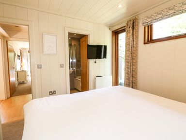 A bedroom with a bed a wall mounted television a door to a bathroom and a window with curtains at Brooke Exton Rutland
