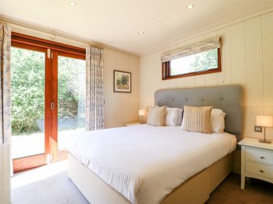 A bedroom with a large bed two nightstands lamps and glass doors opening to a garden at Brooke in Exton Rutland