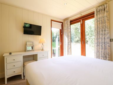 A bedroom with a white desk a stool a lamp a TV and large windows with curtains at Brooke in Exton Rutland