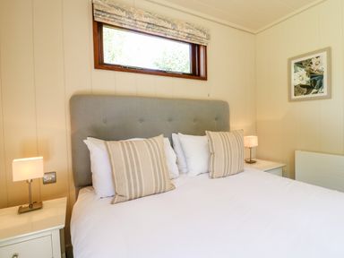 A bed with gray headboard and striped cushions between two bedside tables with lamps in a bedroom at Brooke in Exton Rutland