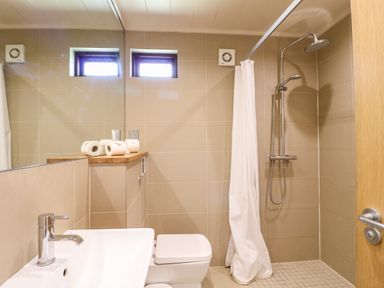 A bathroom with a sink toilet shower area with a curtain and several rolls of toilet paper on a shelf at Brooke in Exton Rutland