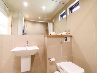 A bathroom with a wall-mounted sink a toilet a shower area with a curtain and towels on a rack at Brooke in Exton Rutland