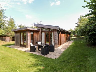 A wooden house with large glass doors and outdoor furniture on a stone patio surrounded by grass at Brooke in Exton Rutland