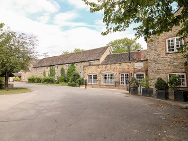 Exterior view of stone buildings with multiple windows and a reception sign surrounded by trees and plants at Brooke in Exton Rutland