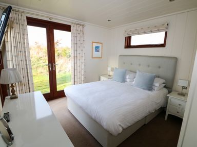 A bedroom with a double bed two bedside tables and a window beside French doors at Burley in Exton Rutland