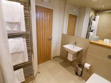 A bathroom with a wooden door a wall-mounted sink a mirror a towel rack with white towels and a small trash bin at Burley in Exton Rutland