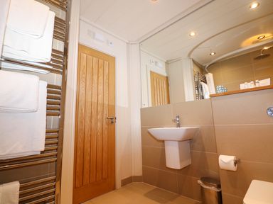 A bathroom with a wooden door a towel rack with white towels a wall-mounted sink a mirror and a shower at Burley in Exton Rutland