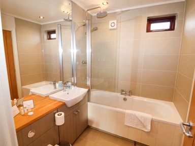 A bathroom with a bathtub and shower combination a sink with wooden countertop and a large mirror at Burley in Exton Rutland