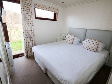 A bedroom with a double bed pillows bedside table lamp window and door overlooking a garden at Burley in Exton Rutland