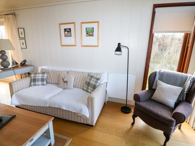 A living room with a striped sofa and patterned pillows next to an armchair with a cushion and throw blanket at Burley in Exton Rutland