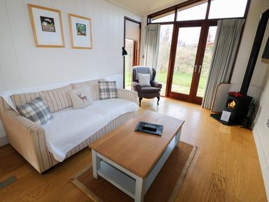 A living room with a sofa, armchair, wooden coffee table, wood stove, and glass doors leading outside at Burley in Exton Rutland