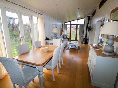 A dining area with six chairs and a wooden table next to glass doors and a living area with sofa armchair coffee table and fireplace at Burley in Exton Rutland