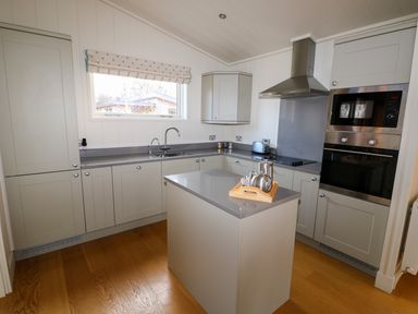 A kitchen with a central island a window above the sink and built in oven and microwave at Burley in Exton Rutland