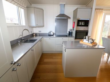 A kitchen with gray countertops white cabinets a stainless steel oven and microwave and a kitchen island with tea set at Burley in Exton Rutland