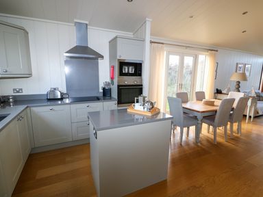A kitchen with an island countertop next to a dining table with six chairs by glass doors at Burley in Exton Rutland