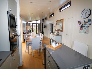 A dining area with a wooden table and six chairs next to a kitchen island with a tray of utensils and appliances at Burley in Exton Rutland