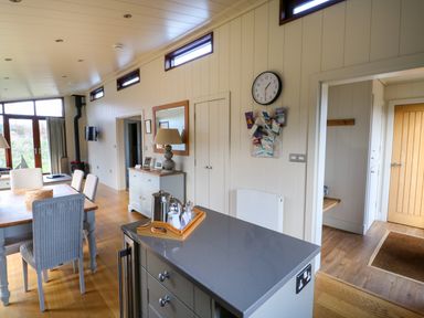 A dining area with a wooden table and chairs next to a kitchen island with a tray of tea items and a wall clock at Burley in Exton Rutland