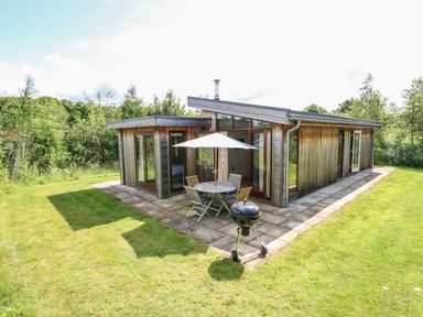 A small wooden outdoor patio with table chairs umbrella and barbecue grill at Burley in Exton Rutland
