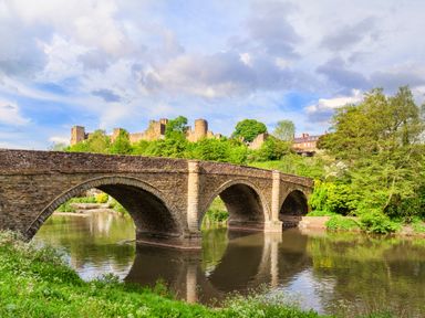 A stone arched bridge over a river with trees and a castle in the background at Shepherds Cabin at Titterstone in Clee Hill