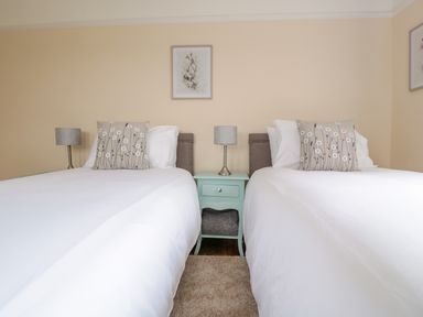 A bedroom with two beds white bedding floral pillows a green nightstand and two lamps at Bower View in Madley