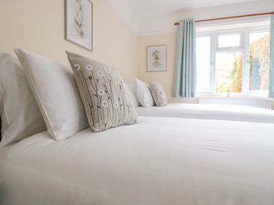 Two beds with white linens and floral decorative pillows near a window with blue curtains at Bower View in Madley