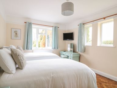 A bedroom with two beds a wall-mounted TV a desk and windows with curtains at Bower View in Madley