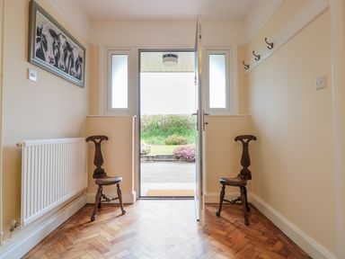 An entryway with two wooden chairs a radiator a painting of cows and an open door at Bower View in Madley