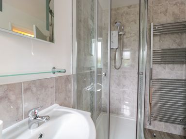 A bathroom with a sink, glass shelf, a shower enclosure, and a heated towel rail at Bower View in Madley