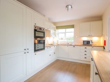 A kitchen with white cabinets wood countertops an oven a microwave and a window with a green blind at Bower View in Madley