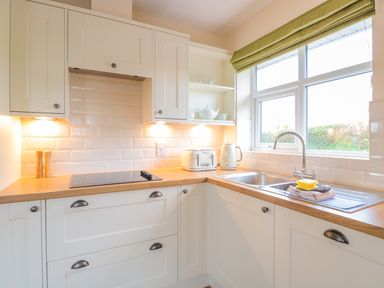 A kitchen with white cabinets a wooden countertop a stove a toaster kettle and a sink under a window at Bower View in Madley